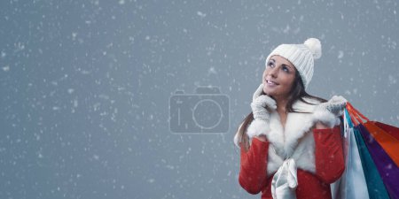 Photo for Happy woman doing Christmas shopping under the snow, she is smiling and holding many bags - Royalty Free Image