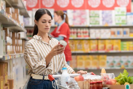 Foto de Mujer sosteniendo una lata y leyendo una etiqueta de información nutricional en el supermercado, compras de comestibles y concepto de nutrición - Imagen libre de derechos