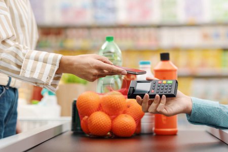 Téléchargez les photos : Femme payant ses courses au supermarché, elle met son smartphone sur le terminal POS, concept de paiement mobile - en image libre de droit