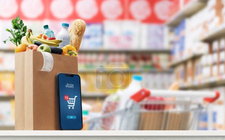 Foto de Bolsa de comestibles llena de productos y aplicación de compras de comestibles en una pantalla de teléfono inteligente, interior del supermercado en el fondo - Imagen libre de derechos