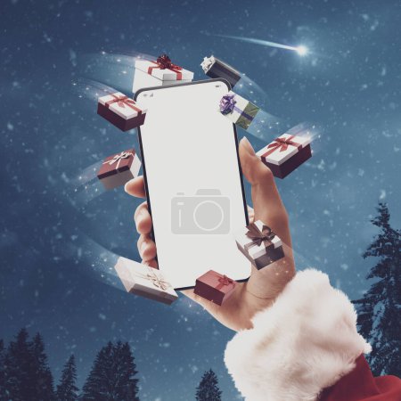 Photo for Santa Claus holding a smartphone with blank screen surrounded by Christmas gifts, snow falling in the background, online shopping concept - Royalty Free Image