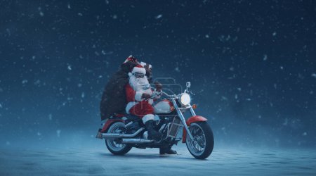 Coole Biker Weihnachtsmann posiert auf einem schnellen Motorrad unter dem Schnee und trägt einen Sack mit Geschenken