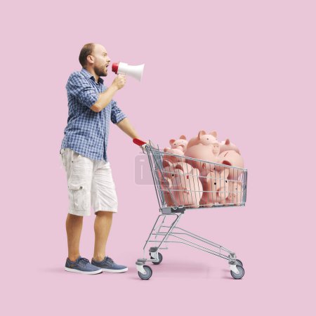 Photo for Man shouting into a megaphone and pushing a shopping cart full of piggy banks, shopping on a budget and discounts concept - Royalty Free Image