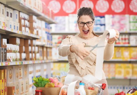 Téléchargez les photos : Femme faisant de l'épicerie au supermarché, elle coupe un long reçu d'épicerie : prix réduit, rabais et concept d'épicerie abordable - en image libre de droit