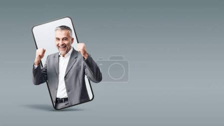 Foto de Cheerful successful businessman in a smartphone videocall and smiling, online  service concept - Imagen libre de derechos