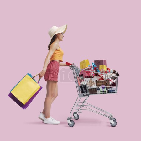 Téléchargez les photos : Joyeux shopaholic femme poussant un panier plein de cadeaux, vente et concept d'achat - en image libre de droit