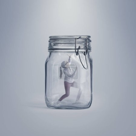 Photo for Scared young woman trapped in a huge glass jar, she is desperate and unable to escape - Royalty Free Image