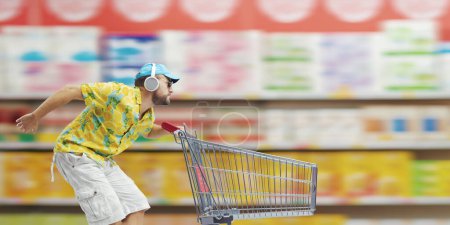 Photo for Cool guy running and pushing a supermarket trolley, grocery shopping and offers concept - Royalty Free Image