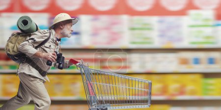 Photo for Senior explorer doing grocery shopping, he is running and pushing a shopping cart at the supermarket - Royalty Free Image