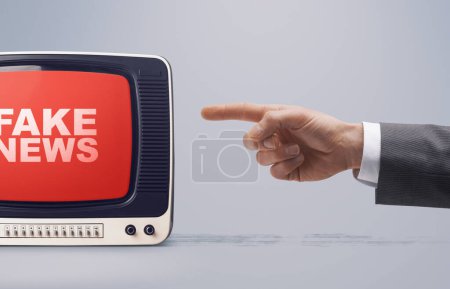 Photo for Hand pointing at an old television broadcasting false information: fake news exposure concept - Royalty Free Image