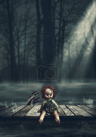 Téléchargez les photos : Poupée effrayante sur une terrasse en bois la nuit, une main de zombie se lève derrière elle : concept d'horreur et de mystère - en image libre de droit