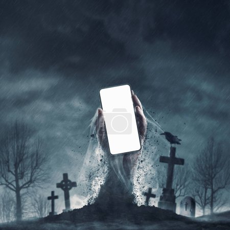 Foto de Espantosa mano zombi saliendo de una tumba y sosteniendo un teléfono inteligente con pantalla en blanco, espacio de copia - Imagen libre de derechos