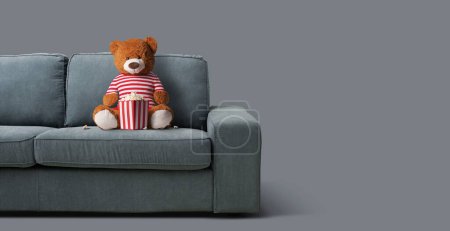 Foto de Osito de peluche sentado en el sofá y viendo películas en casa - Imagen libre de derechos