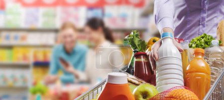Photo for Woman putting fresh groceries in the shopping cart at the grocery store, grocery shopping and retail concept, copy space - Royalty Free Image