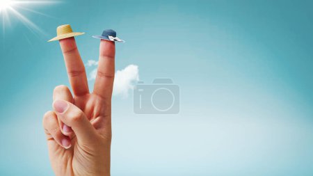 Foto de Mano femenina haciendo un signo de V y usando pequeños sombreros de playa en dos dedos, cielo azul en el fondo, concepto de vacaciones de verano - Imagen libre de derechos