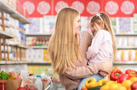Foto de Retrato de una madre feliz sosteniendo a su hija en la tienda de comestibles, que están sonriendo el uno al otro, compras de comestibles y el concepto de estilo de vida - Imagen libre de derechos