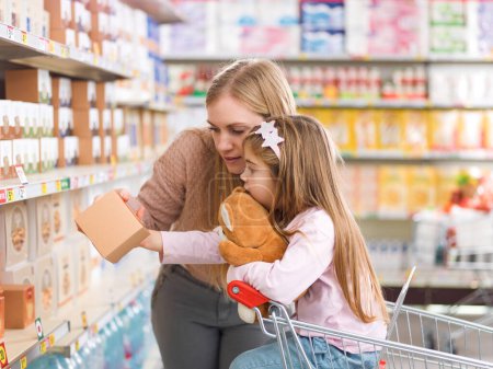 Téléchargez les photos : Jolie famille heureuse faisant des courses au supermarché : une mère et sa fille choisissent des épiceries sur l'étagère du magasin - en image libre de droit