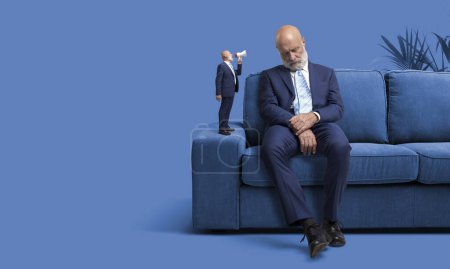 Hombre de negocios mayor durmiendo en el sofá en casa, una versión más pequeña de sí mismo le está gritando usando un megáfono y despertándolo