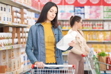 Photo for Woman doing grocery shopping at the supermarket, she is checking the label on a bottle of detergent - Royalty Free Image