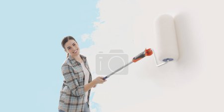 Photo for Happy woman painting walls in her new home, she is using a paint roller, banner with copy space - Royalty Free Image