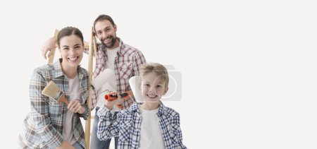 Foto de Familia feliz con un niño joven renovando su casa, están pintando paredes y sonriendo a la cámara - Imagen libre de derechos