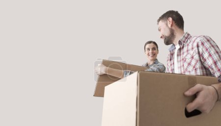 Photo for Young smiling couple moving into a new house, they are carrying full cardboard boxes - Royalty Free Image
