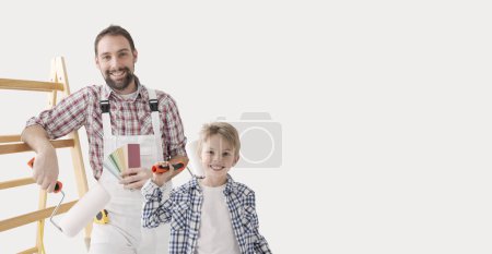 Foto de Padre e hijo pintando juntos su nuevo hogar, están sosteniendo rodillos de pintura y sonriendo a la cámara - Imagen libre de derechos