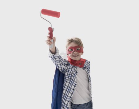 Téléchargez les photos : Superhéros mignon garçon portant un costume et tenant un rouleau de peinture, décoration à la maison et concept de peinture - en image libre de droit