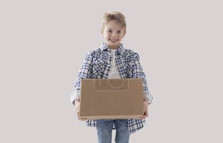 Téléchargez les photos : Joyeux garçon fort tenant une grande boîte en carton, concept de livraison et de déménagement à domicile - en image libre de droit
