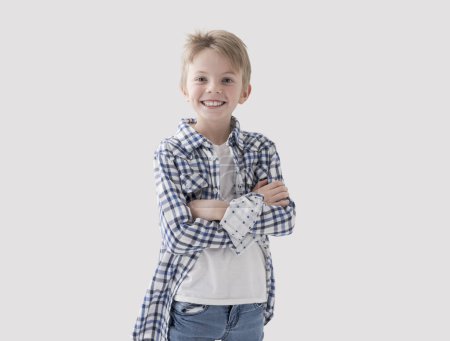 Téléchargez les photos : Mignon heureux blonde garçon posant avec les bras croisés et souriant, fond blanc - en image libre de droit