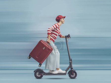 Téléchargez les photos : Femme touristique chevauchant un scooter électrique rapide et portant un sac trolley, concept de mobilité durable - en image libre de droit