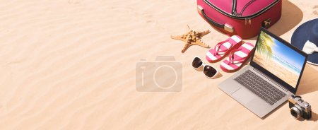 Téléchargez les photos : Sac de voyage, accessoires de plage et ordinateur portable sur le sable, concept de vacances d'été - en image libre de droit