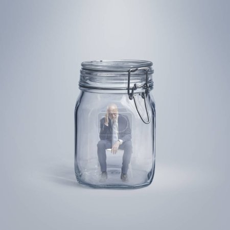Foto de Hombre de negocios superior sin esperanza atrapado dentro de un frasco de vidrio, él está sentado y pensando, el aislamiento y el concepto de fracaso - Imagen libre de derechos