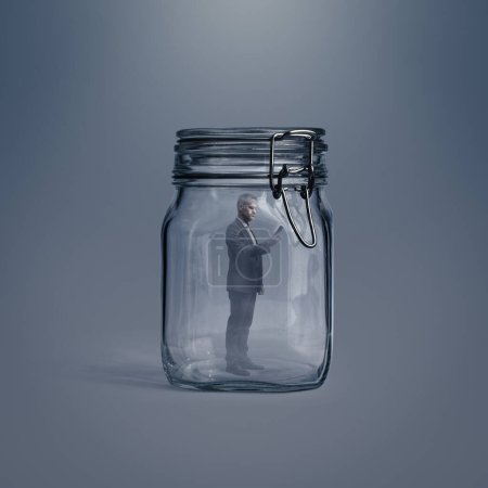 Foto de Empresario corporativo atrapado dentro de un frasco de vidrio, que está utilizando un teléfono inteligente - Imagen libre de derechos