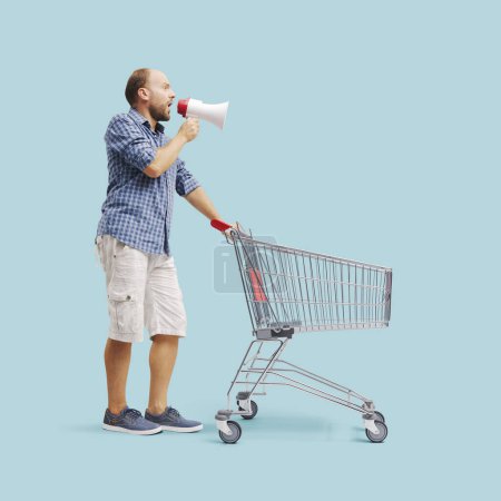 Photo for Loud man shouting into a megaphone and pushing an empty shopping cart: marketing, offers and sale concept - Royalty Free Image