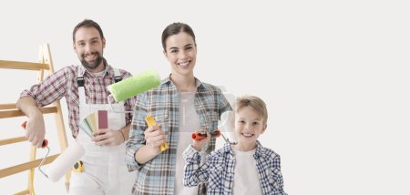 Téléchargez les photos : Famille peignant leur nouvelle maison, ils tiennent des rouleaux de peinture et sourient à la caméra - en image libre de droit
