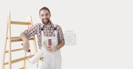 Foto de Pintor profesional confiado posando, está sosteniendo un rodillo de pintura y muestras de color, renovación del hogar y concepto de decoración - Imagen libre de derechos