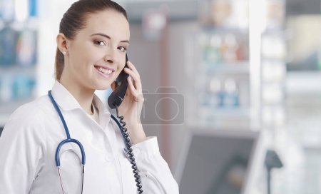 Téléchargez les photos : Pharmacienne professionnelle travaillant à la pharmacie, elle reçoit un appel téléphonique et donne des conseils - en image libre de droit