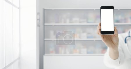 Téléchargez les photos : Pharmacien montrant un smartphone avec écran blanc à la pharmacie : commander des médicaments en ligne - en image libre de droit