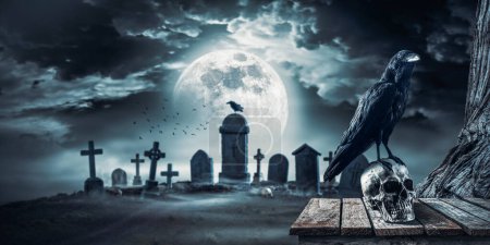 Foto de Antiguo cementerio espeluznante en la noche con cuervo espeluznante de pie sobre un cráneo humano, luna llena en el fondo: horror y concepto de Halloween - Imagen libre de derechos