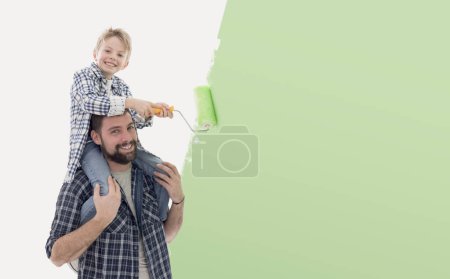Téléchargez les photos : Jeune père et mignon garçon posant ensemble et souriant, ils peignent leur nouvelle maison ensemble - en image libre de droit