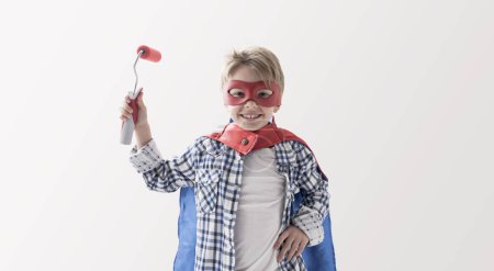 Foto de Lindo niño superhéroe usando un traje y sosteniendo un rodillo de pintura, decoración casera y concepto de pintura - Imagen libre de derechos