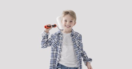 Téléchargez les photos : Mignon garçon créatif tenant un rouleau de peinture et souriant, concept de peinture et de décoration à la maison - en image libre de droit