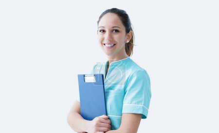 Téléchargez les photos : Jeune infirmière travaillant à l'hôpital, elle tient des dossiers médicaux et sourit - en image libre de droit