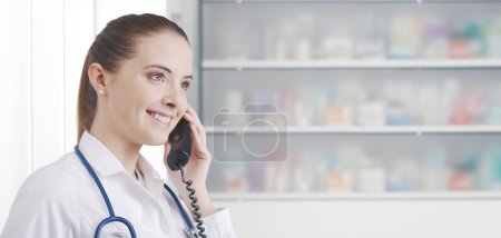 Téléchargez les photos : Pharmacienne professionnelle travaillant à la pharmacie, elle reçoit un appel téléphonique et donne des conseils - en image libre de droit