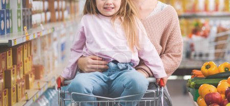 Téléchargez les photos : Jolie fille mignonne souriant et faisant des courses avec sa mère au supermarché, style de vie et concept de famille - en image libre de droit