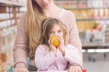Photo for Lovely girl doing grocery shopping with her mother, she is holding a fresh orange - Royalty Free Image