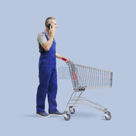 Photo for Professional repairman pushing an empty shopping cart and having a phone call - Royalty Free Image