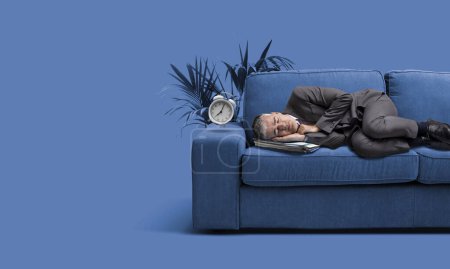 Téléchargez les photos : Homme d'affaires d'entreprise sieste sur un canapé et deux cloches réveil sonner - en image libre de droit