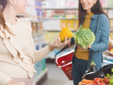 Photo for Happy women meeting at the supermarket, they are talking and buying fresh healthy vegetables together, grocery shopping and lifestyle concept - Royalty Free Image